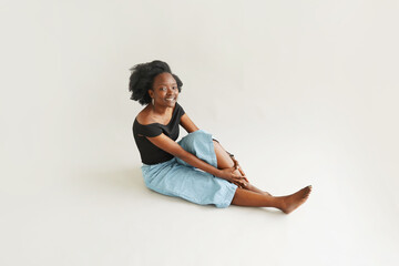 Cheerful Young African American Woman Sitting on the Floor on White Background In Studio