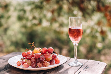 A glass of champagne or wine next to pink grapes is placed on a wooden table against a background of pine and juniper forests
