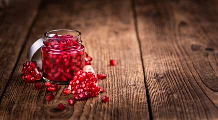 Some fresh preserved Pomegranate seeds on wooden background (selective focus; close-up shot)
