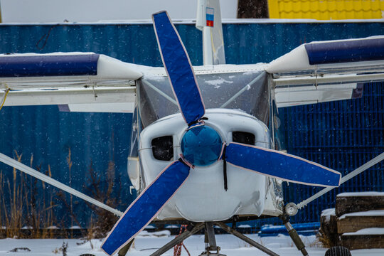 small aircraft with a propeller painted in bright colors in a case at the airfield or airport in the snow in winter