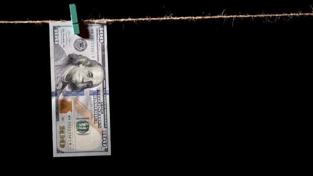 Money laundering concept. AML. Money hanging on a rope on black background. Washed dollars drying clipped with pegs. Stock footage of money laundering and cleaning dirty money financial concept