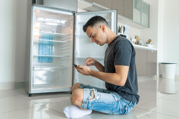 A young guy orders food using a smartphone. Empty refrigerator with no food. Food delivery service advertisement
