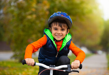 Naklejka premium Portrait of a boy in the park. Small child wearing a helmet and cycling on an autumn day. Active healthy outdoor sports