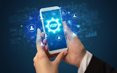 Female hand holding smartphone with VOIP abbreviation, modern technology concept