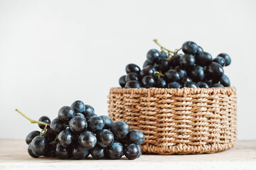 Bunch of black grapes in a round wicker basket on a old wooden table. Copy, empty space for text