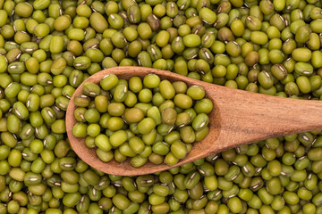 Mung beans in background and on wooden spoon seen directly from above covering the full frame