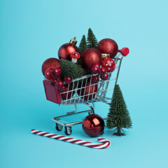 Christmas and New Year shopping layout made with trolley, tree, candy cane and ornaments on bright blue background. Minimal winter December sale or shopping mall concept. 