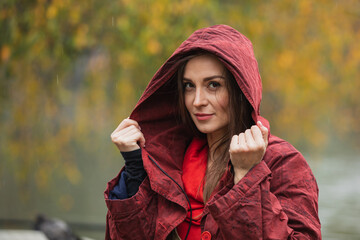 Portrait of a woman in hooded red raincoat walking in park on a rainy day