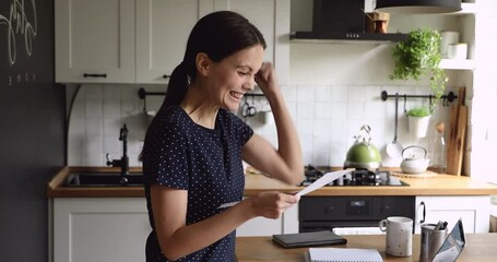 Side head shot view curious young girl reading paper letter, celebrating university admission or getting grant scholarship notification, feeling euphoric alone in kitchen, making yes I did it gesture.