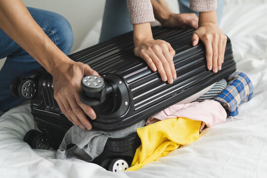 couple trying to close overload suitcase because too many things in the luggage.