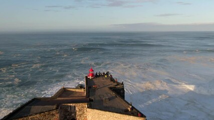 Aerial view of historical landmark Fort of Sao Miguel Arcanjo Lighthouse at sunrise in Nazare, Portugal. Nazare is famously known to surfers for having the largest waves in the world.