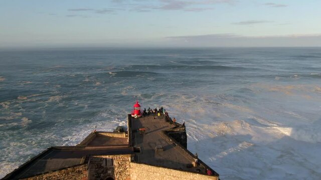 Aerial view of historical landmark Fort of Sao Miguel Arcanjo Lighthouse at sunrise in Nazare, Portugal. Nazare is famously known to surfers for having the largest waves in the world. - Powered by Adobe