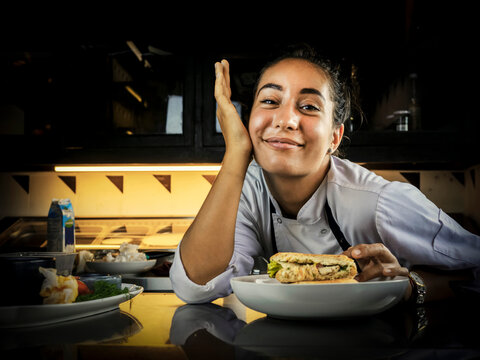 Closeup image of a female chef cooking and holding a piece of whole wheat sandwich in kitchen