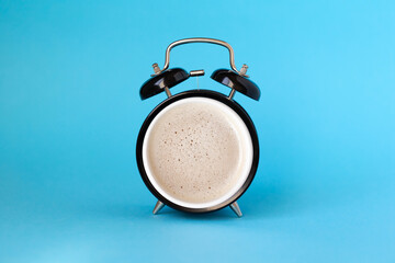 Wake up concept: alarm clock and cup of coffee mixed in one on blue background