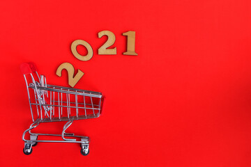 Shopping cart and numbers in gold color 2021 on a red background with a copy of the space. Christmas online shopping.