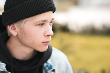 Stylish teen boy 15-16 year old wearing black knitted hat and hoodie outdoors close up. Autumn season. Teenagerhood.