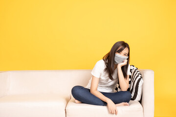 Fototapeta na wymiar Young asian woman wearing face mask resting on the sofa at yellow background