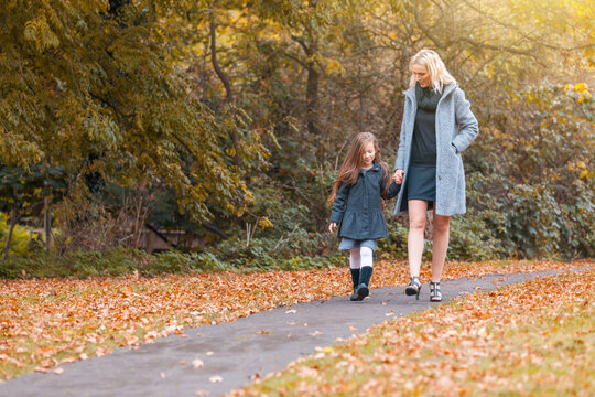 Mother and daughter at park in autumn in London - Happy mom and girl wearing warm clothes on a funny day out together - fall season lifestyle image