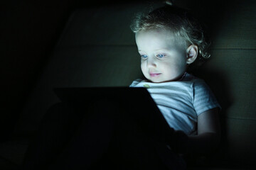 Little girl watching cartoons on a tablet in the dark
