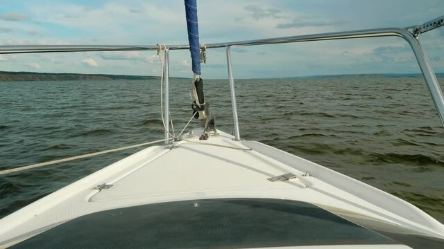 Curtailed sail and jib furler on yacht sailing on river Volga. Water surface and sky are on backgorund.