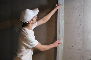 master applies the rule to the wall, checking laser level, applies the marking