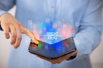 Young man holding a foldable smartphone with BRIGHT IDEAS inscription, educational concept