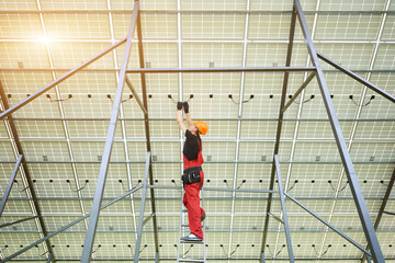 Installing and wiring of solar photo voltaic panel. Worker in orange uniform connects solar panels at the station. Ecology power conservation concept.