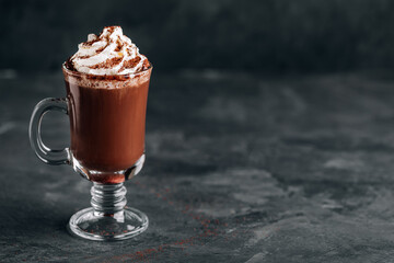 Hot chocolate cocoa with whipped cream in glass on dark background, copy space.