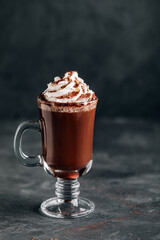 Hot chocolate cocoa with whipped cream in glass on dark background, copy space.