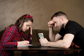 A man holds money and watches his wife calculate the budget. The difficulties of a young family, the financial crisis