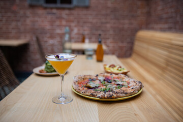 Vegan pizza, a cocktail, and other vegan dishes on a wooden restaurant table