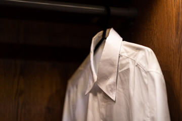 A formal white cotton shirt is hanging in wooden wardrobe. Isolated object and selected focus at the part of T-shirt textile. 