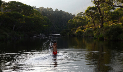 Fototapeta na wymiar Kid splashes water in Thredbo River at Kosciuszko National Park, NSW Australia. 