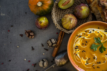 Obraz na płótnie Canvas Autumn menu. Top view photo of bowl with pumpkin soup, gem squashes, rosemary, pepper, fresh baked bread and silver spoon. Dark grey textured background. Healthy eating concept. 