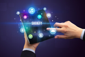 Businessman holding a foldable smartphone with SOCIETY inscription, social media concept