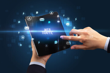 Businessman holding a foldable smartphone with WEB TRAFFIC inscription, social networking concept
