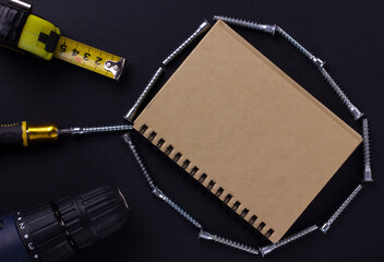 tools for repair and construction. Screwdriver, measuring tape, furniture screws, notebook on a black background with a place for text. View from above