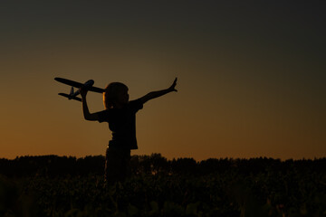 Fototapeta na wymiar Silhouette of boy playing with airplane in the field