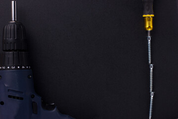 the background for the text is made of furniture screws, a screwdriver, a screwdriver on a black background (top view).