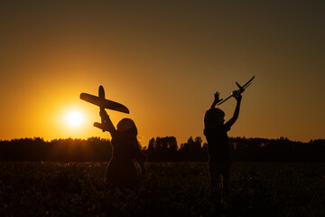 Fototapeta na wymiar Silhouettes of kids playing with airplane in the field