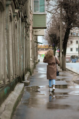 A beautiful young woman runs down the street after the rain. Back girl