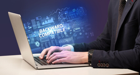 Businessman working on laptop with BACKWARD COMPATIBLE inscription, cyber technology concept