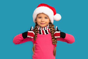 A little girl in a Christmas hat poses on a blue background for the new year.