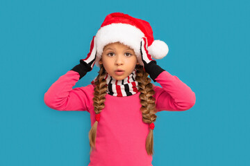 A little girl in a Christmas hat poses on a blue background for the new year.