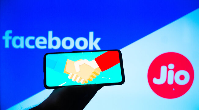 Mobile phone with a handshake screen and facebook and jio in the background