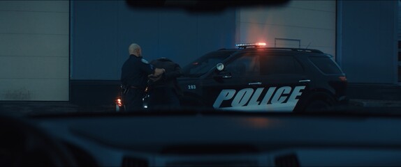 WIDE Police officer searches and handcuffs a suspect, African-American Black criminal. Police car lights flashing in the background