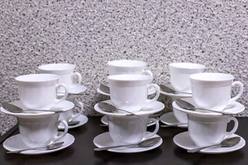 Many empty white cups with spoons stand on the table.