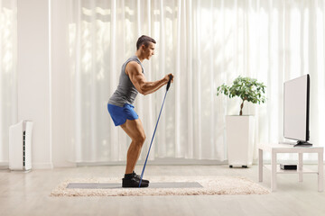 Fototapeta premium Guy exercising with a resistance band at home while watching tv
