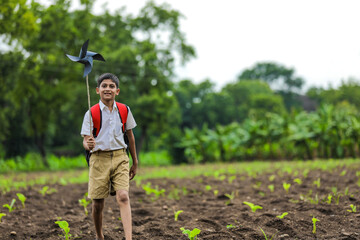 Cute indian child holding school bag and playing with pinwheel on road side
