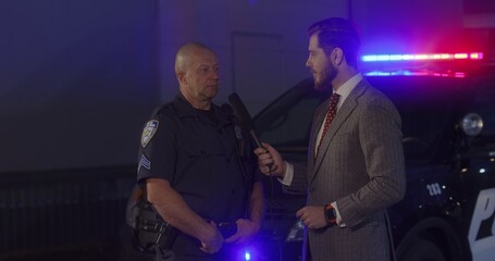 FIXED Reporter conducts interview with police representative on a crime scene. Police car lights flashing in the background. Model released for commercial use